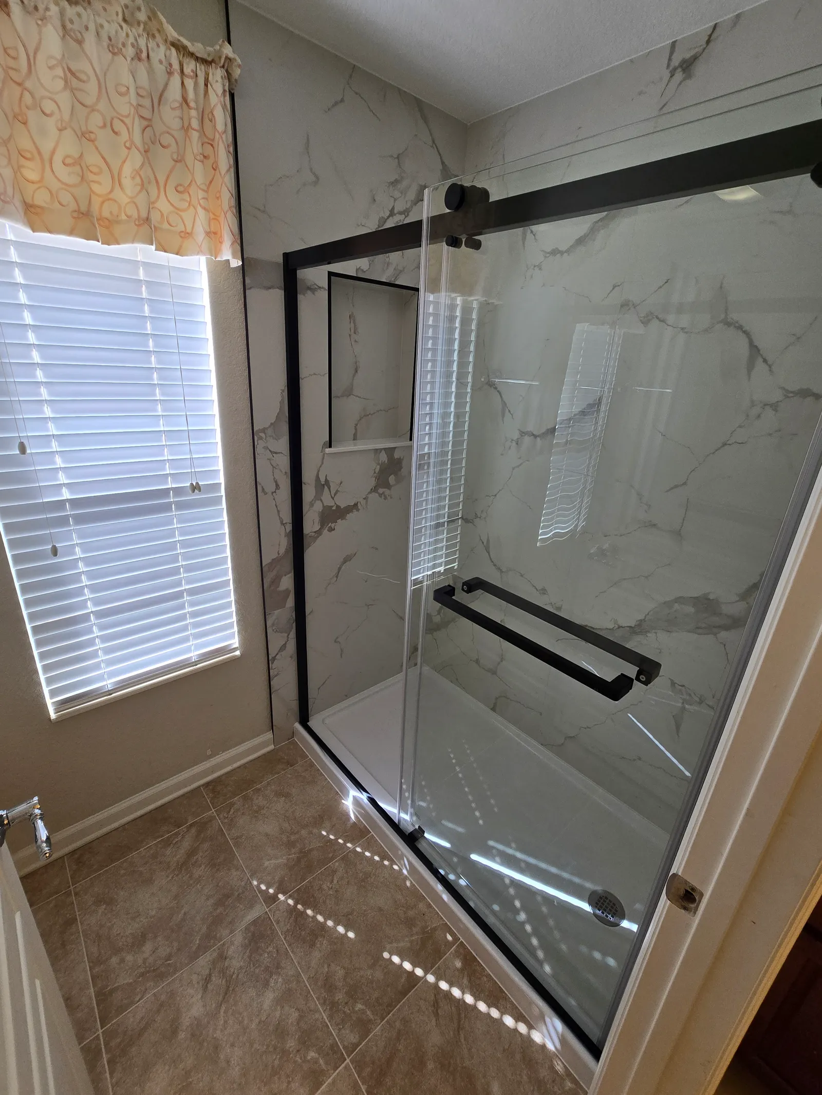 New shower with black-frame sliding glass and marble-look porcelain walls