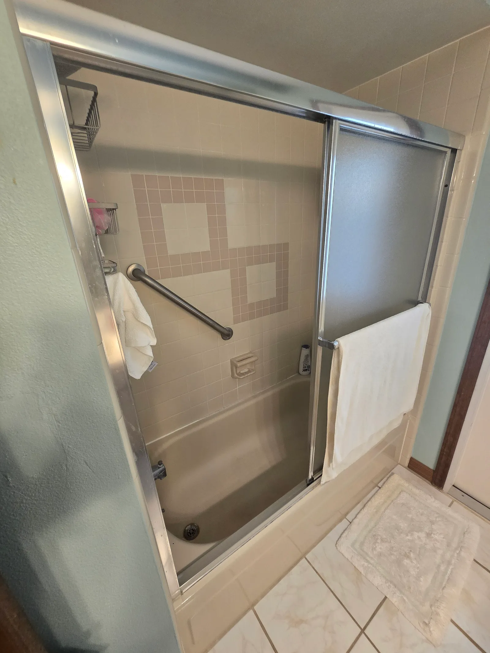 Dated tub and shower with grab bar and sliding door before the remodel