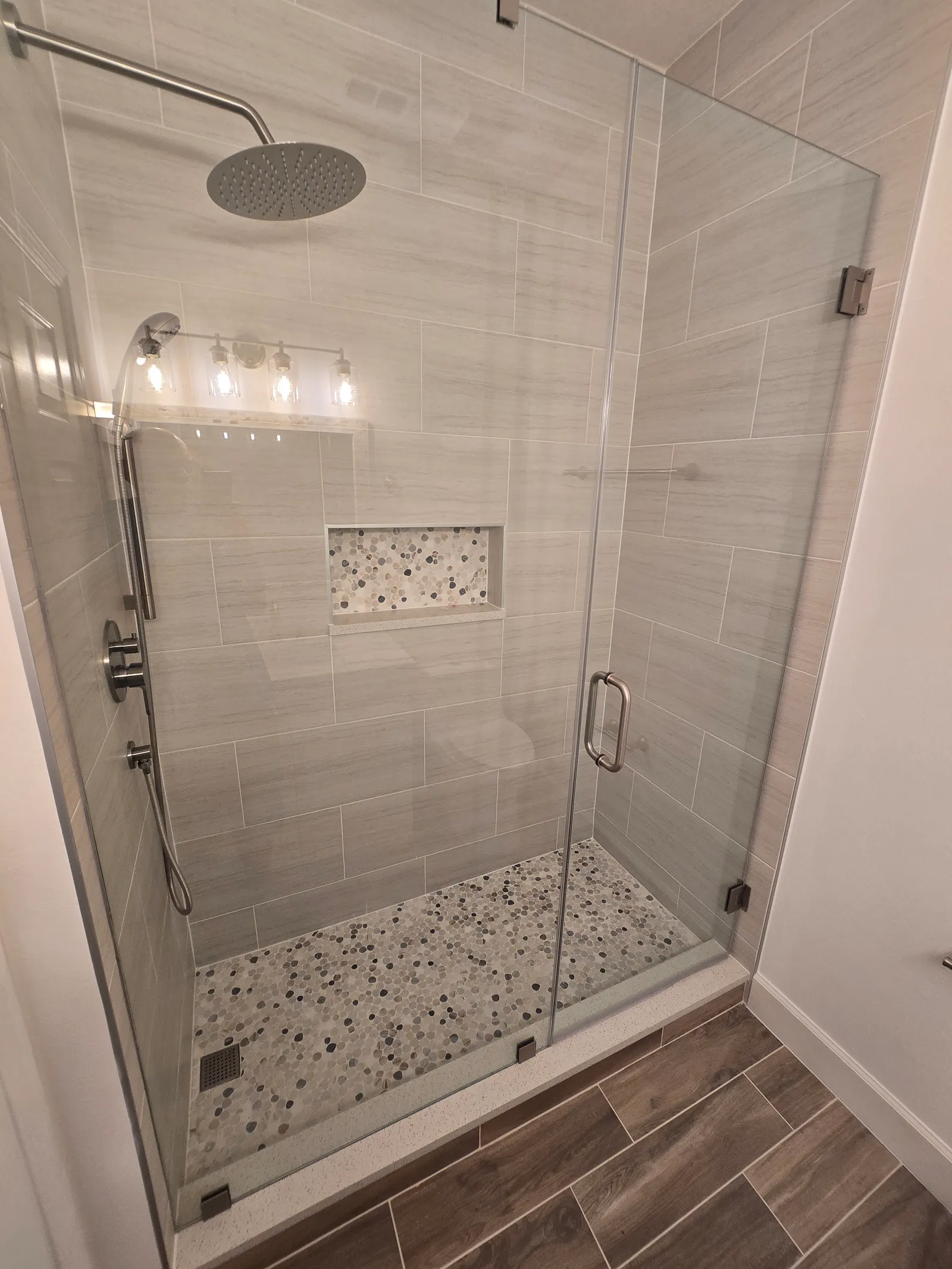 Walk-in shower with frameless glass door, light stone-look tile and pebble mosaic floor after the conversion