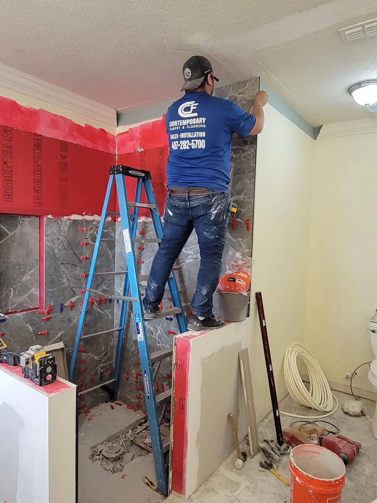 Contemporary crew member on a ladder setting large-format marble-look tile over red waterproofing membrane