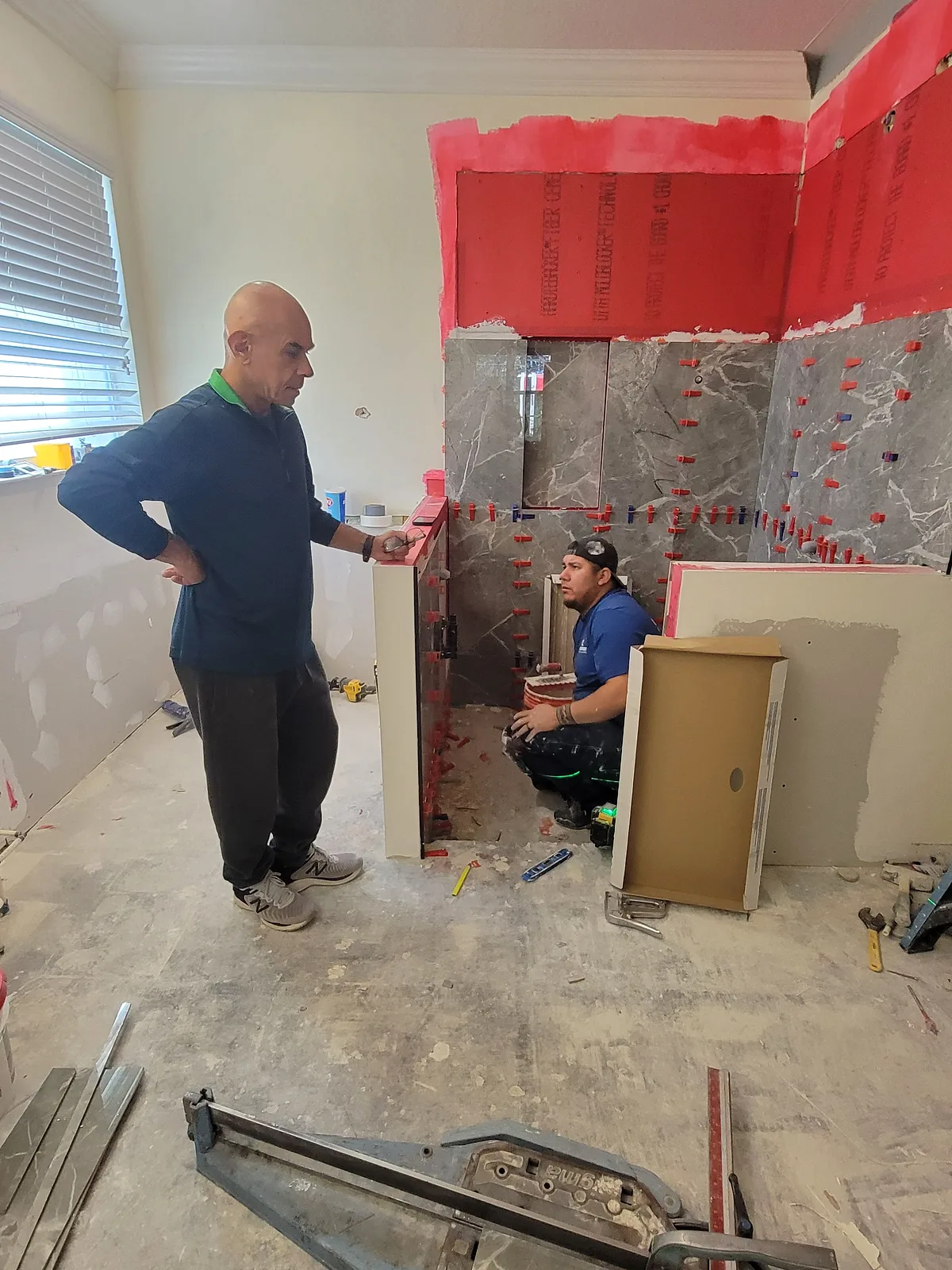 The two-person crew working in a bathroom stripped to the studs, membrane and cement board already up