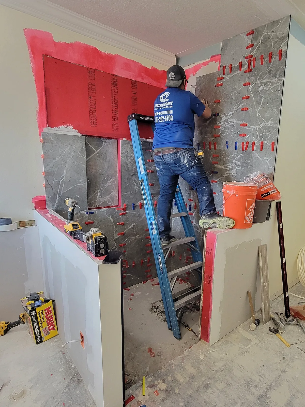 Contemporary crew member tiling a shower wall with the red waterproofing membrane still exposed above it