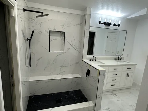 Marble-look shower with black fixtures beside a white double vanity