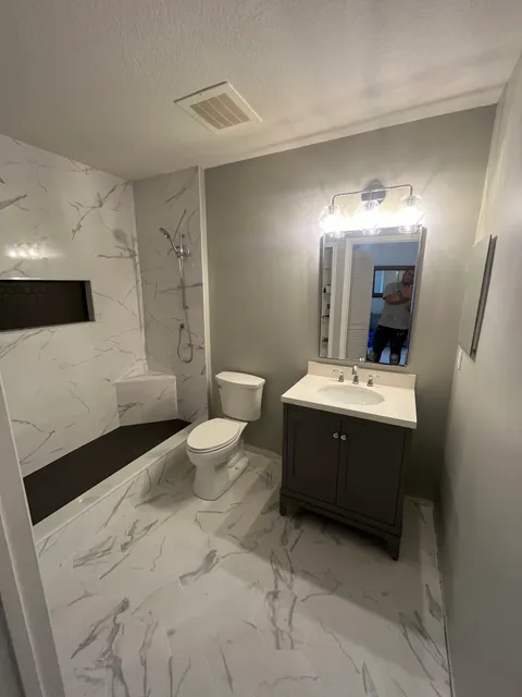Full bathroom with marble-look shower, dark vanity and framed mirror