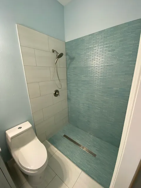 Teal glass tile shower with gray plank tile wall and chrome fixtures