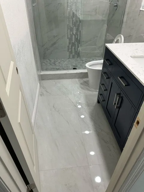 Frameless glass shower, toilet and navy vanity on marble floor