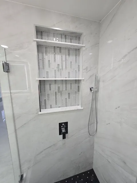 Marble shower with vertical mosaic niche and black hexagon floor