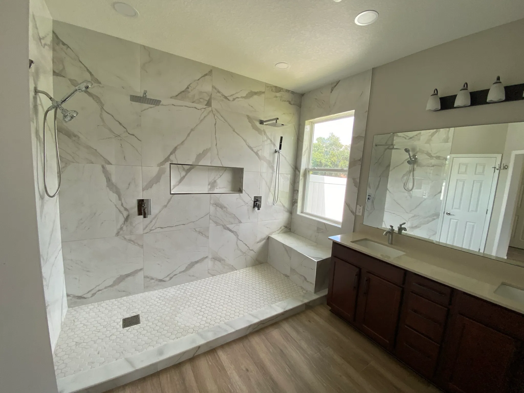 Walk-in shower with marble-look porcelain walls, bench, niche and window