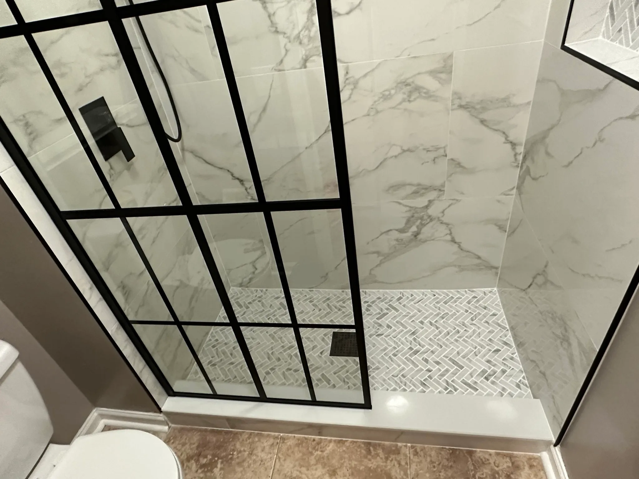 Tub-to-shower conversion with black-frame grid glass and marble-look tile