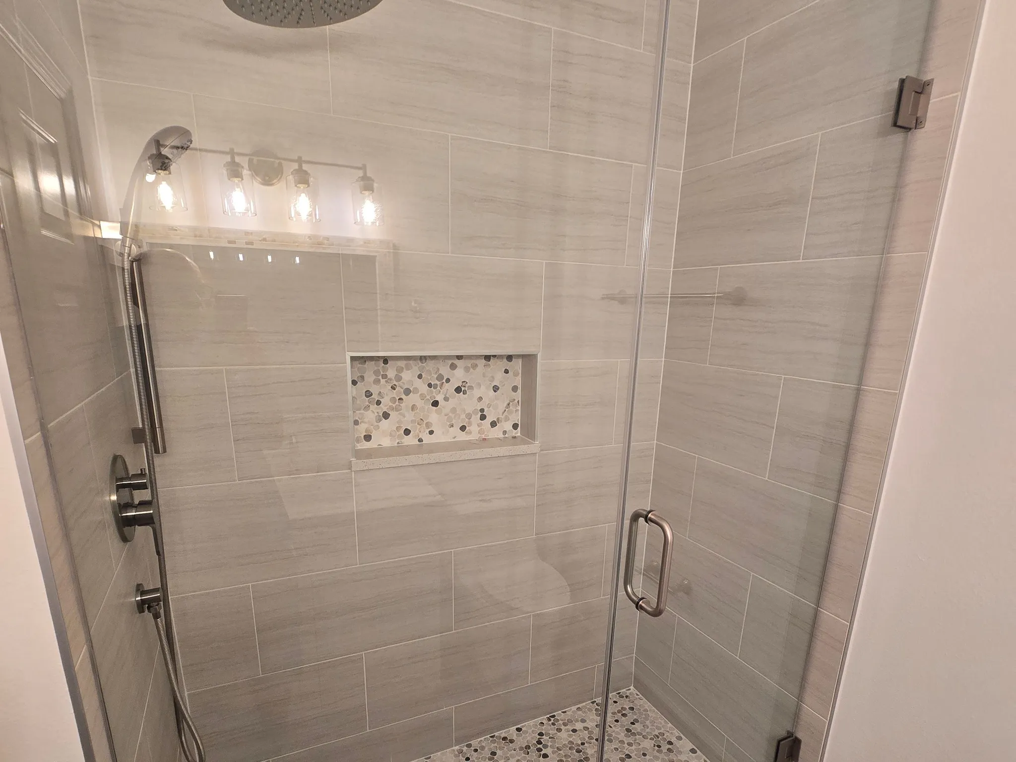 Guest bathroom walk-in shower with frameless glass door, light stone-look tile and pebble mosaic floor