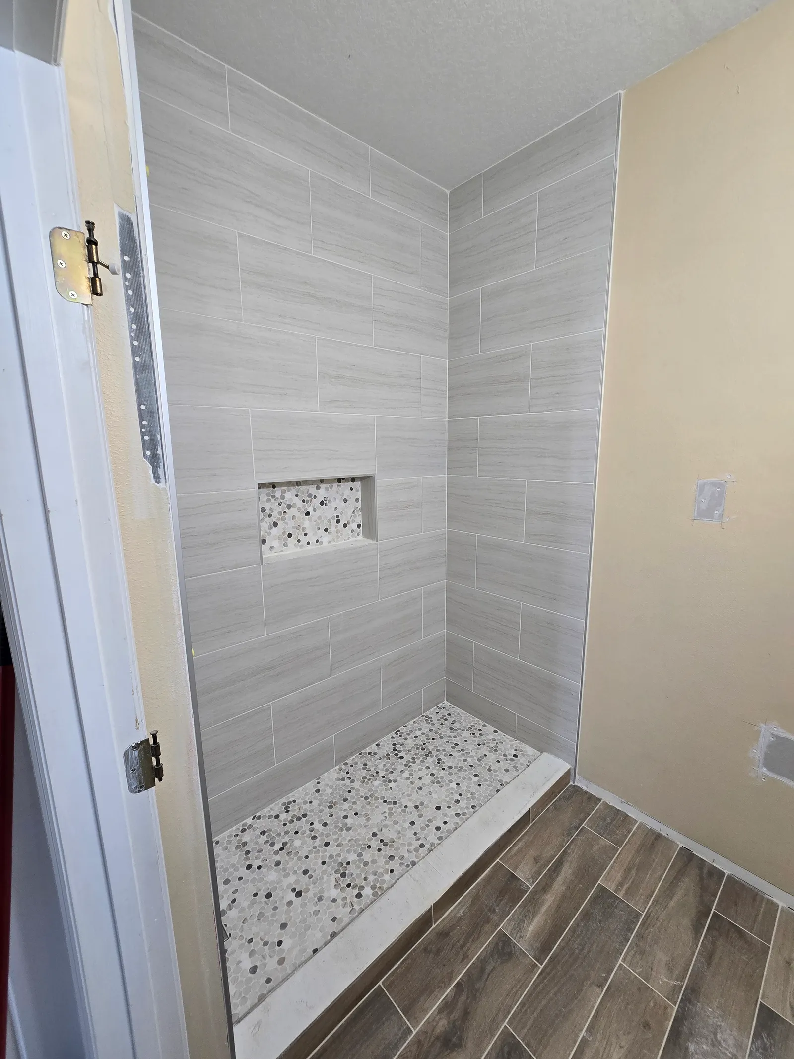 Tiled walk-in shower with pebble floor and mosaic niche before glass and fixtures