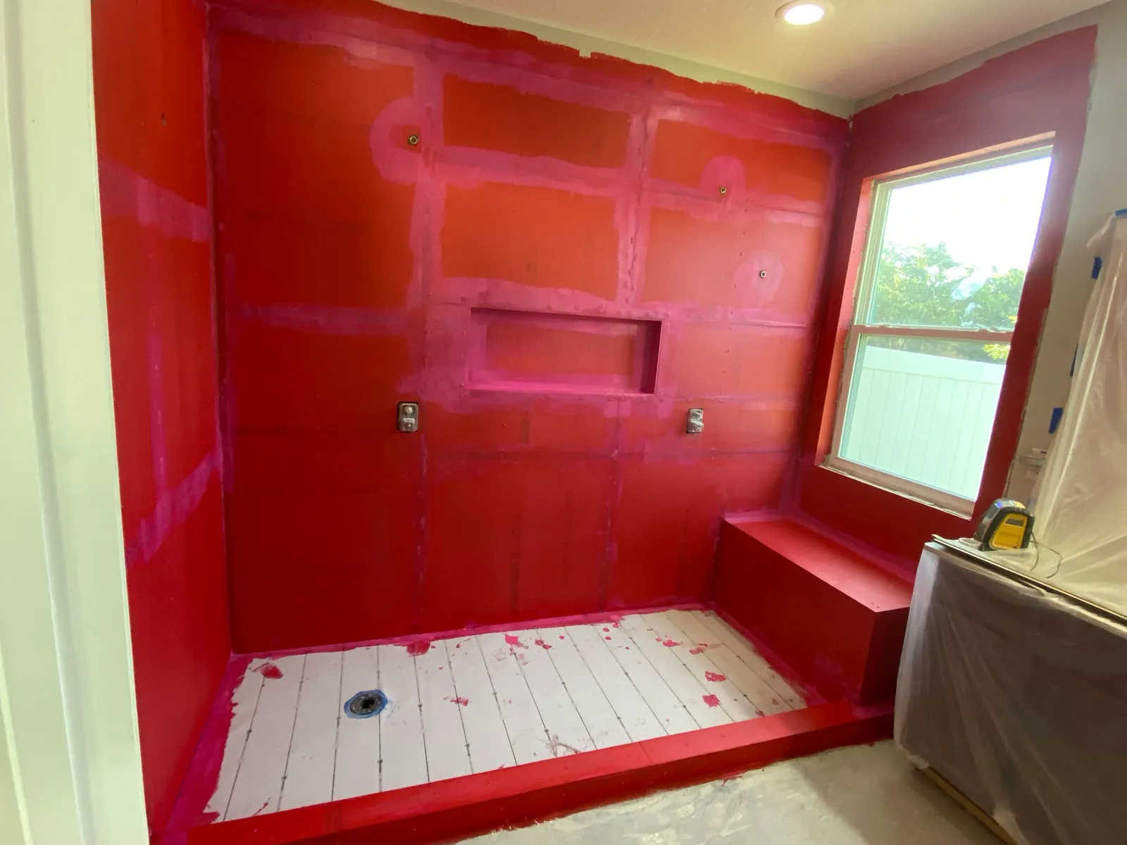 Shower walls, bench and pan coated in red liquid waterproofing membrane